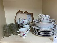 Wide angle showing glass drinking mugs and stacked Premier floral china plates, bowls, and teacups.