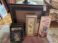 Photo showing variety of framed prints including floral and portrait images and many empty frames stacked and arranged.