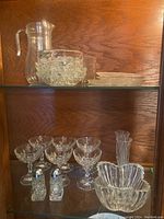 Glassware displayed on two shelves including pitcher, cocktail glasses, champagne flutes, decorative plates, ashtrays, and salt and pepper shakers.
