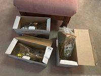 Three brass coach lights packed in original boxes on carpet with partial view of furniture.