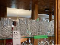 Front view of 8 Mikasa crystal glasses displayed on a glass shelf, showing the faceted and diamond cut design, some with visible chips.