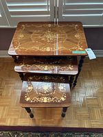 Top view showing three wooden nesting tables stacked, with floral inlay on lacquered tops. Largest table has slight corner damage visible.