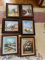 Group photo showing all six framed canvas paintings arranged on carpet, displaying various landscapes and floral still life, some signed