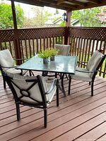 Full set of patio table with four chairs on wooden deck surrounded by railing, showing the table and cushion details.