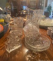 Group of pinwheel pattern glassware including pitcher, vase, ice bucket, candy dishes on wooden table
