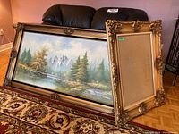 Wide shot showing the framed landscape print and the back of the ornate faux frame leaning to side.