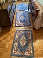 Three acrylic area rugs placed on hardwood floor between dresser and bed, showing relative sizes and patterns.