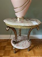 Full view of round side table with manufactured marble top and base, brass-colored trim and legs, supporting large decorative item on top.