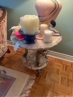 Round side table shown with various candles and a lamp on top, highlighting the manufactured marble top surface, brass-colored trim and legs, and circular marble base.