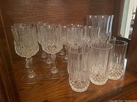 Multiple stemware glasses including champagne flutes and cocktail glasses arranged on wooden shelf