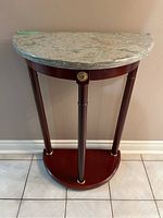 Full front view of the demilune side table showing the full wooden base, legs, and stone top.