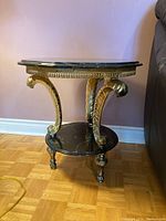 Angle view of two tier table showing black marble top, gold metal frame with decorative scroll legs and claw feet.