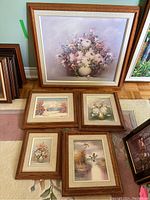 Photo of five paintings arranged on floor. One large floral canvas painting framed in oak with matting and four smaller oak framed and matted paintings including floral arrangements and landscapes.