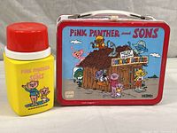 Front and side view of Pink Panther and Sons metal lunchbox along with the matching Thermos showing colorful cartoon characters and branding.