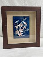 Framed Arita-Yaki porcelain plaque with floral relief against beige backing and wooden shadow box frame showing marks.