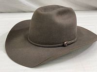 Brown cowboy hat made from pure beaver felt, wide brim, creased crown, thin felt band with metal buckle detail.