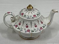 Front and side view of the white ceramic teapot with pink rose design, gold trim, and ribbed body shape.