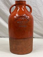 Full view of large decorative pottery jug showing its glossy red top and matte brown base with two side handles.