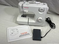 White Singer portable sewing machine model 8280 with foot pedal and instruction manual laid out on surface.