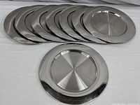 Eight Crate and Barrel stainless steel chargers laid out in a row, polished finish, 13 inch diameter each