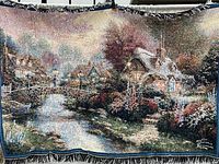 Full view of the woven tapestry throw blanket showing cottage, bridge, and natural setting with detailed weaving and fringe.