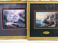 Two framed Thomas Kinkade prints side by side, showing overall condition and matching frames.