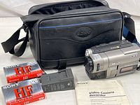 Photo of the camcorder, carry case, battery charger, two Sony HF 120-minute Hi8 tapes, and operating manual arranged on a table.