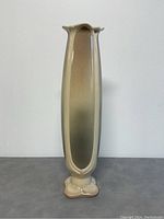 Tall, slender vase with cream to brown gradient glaze photographed against a white background showing front and side details.