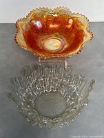 Front top view of two glass bowls placed side by side, showing the iridescent orange Carnival glass and clear Revontulet Ice glass with jagged edges.