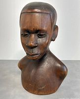 Front and side views of a hand-carved wooden bust of an African male figure showing facial details and wood grain.