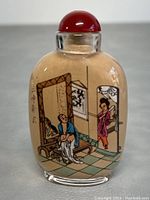 Photo of front side of perfume bottle showing a man seated removing clothing inside an ornate interior with a woman entering through a door.