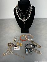Lot consisting of layered necklaces displayed on bust, various bracelets arranged below, and assorted pairs of earrings laid out on table.