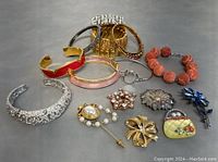 Overall view of assorted bracelets, brooches, and pins laid on a flat surface.