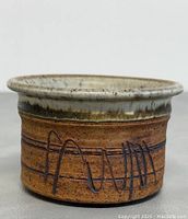 Close-up side view of the handmade pottery showing the brown clay body with incised abstract monogram design and glazed rim.