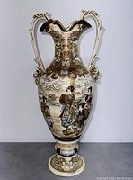 Front view of Japanese style porcelain urn with painted geisha scene, ornate double handles, and scalloped rim.