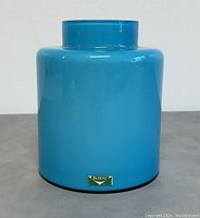 Front angle of blue opaque glass vase with Vistosi label attached near base, showing overall shape and color