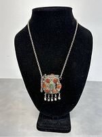 Front view of the necklace on a black display bust showing pendant with colored stones and dangling beads.