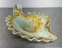 Murano glass decorative dish with ruffled edges and swirl pattern in yellow, green, and white colors. Photo shows side perspective highlighting dish shape and color blending.