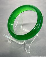 Full view of green jade bangle bracelet displayed on clear stand against gray background