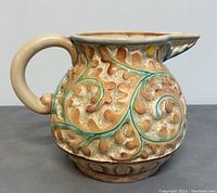 Front and left side view of Beswick oversized ceramic pitcher showing textured leaf and scroll design in earthy colors and bulbous shape with handle and spout.