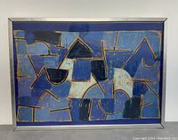 Full front view of framed artwork showing abstract shapes in blues and gold in silver metal frame