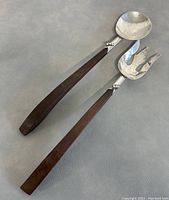 Pair of sterling silver salad servers with long tapered rosewood handles on a gray background