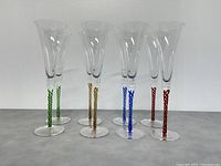Front view of all 8 champagne flutes arranged in pairs by stem color: green, yellow, blue, red.