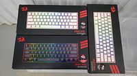 Three boxed Redragon Draconic mechanical keyboards, two with black keycaps and one with white keycaps, showing product images and RGB lighting.