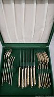 Set of assorted forks arranged on left and right sides inside green presentation case lined with white satin on the lid and green fabric base.