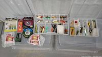 Overview of two clear plastic tackle boxes open showing a variety of fishing lures, lines, lights, and accessories inside various compartments.