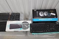 Photo showing four Logitech wireless keyboards, three on the left and one in front of the Gammaxx L240 V2 liquid cooler box on the right.