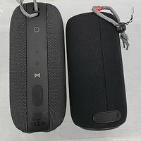 Two black Monster portable speakers showing controls and fabric covering, one with side vertical buttons and other with circular top controls.