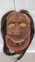 Front view of carved wooden mask showing facial features with horse hair mane or tail attached.