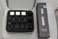 Photo showing one Neewer RGB1 RGB Stick Light box next to open carrying case with three mounted SmallRig stick lights and diffuser caps.